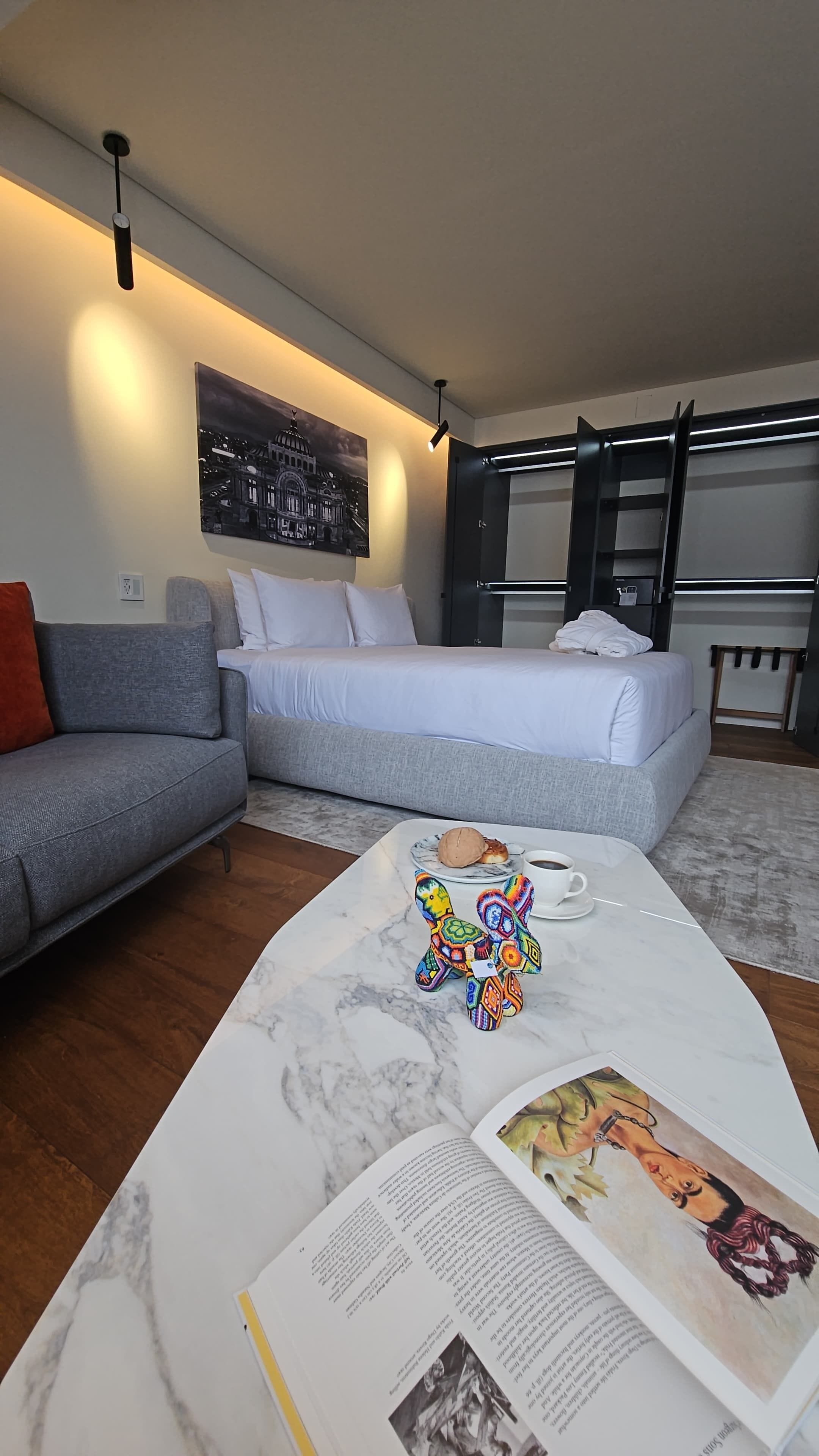 Habitación de hotel moderna con sofá, cama, mesita de centro de mármol y un cuadro en la pared.