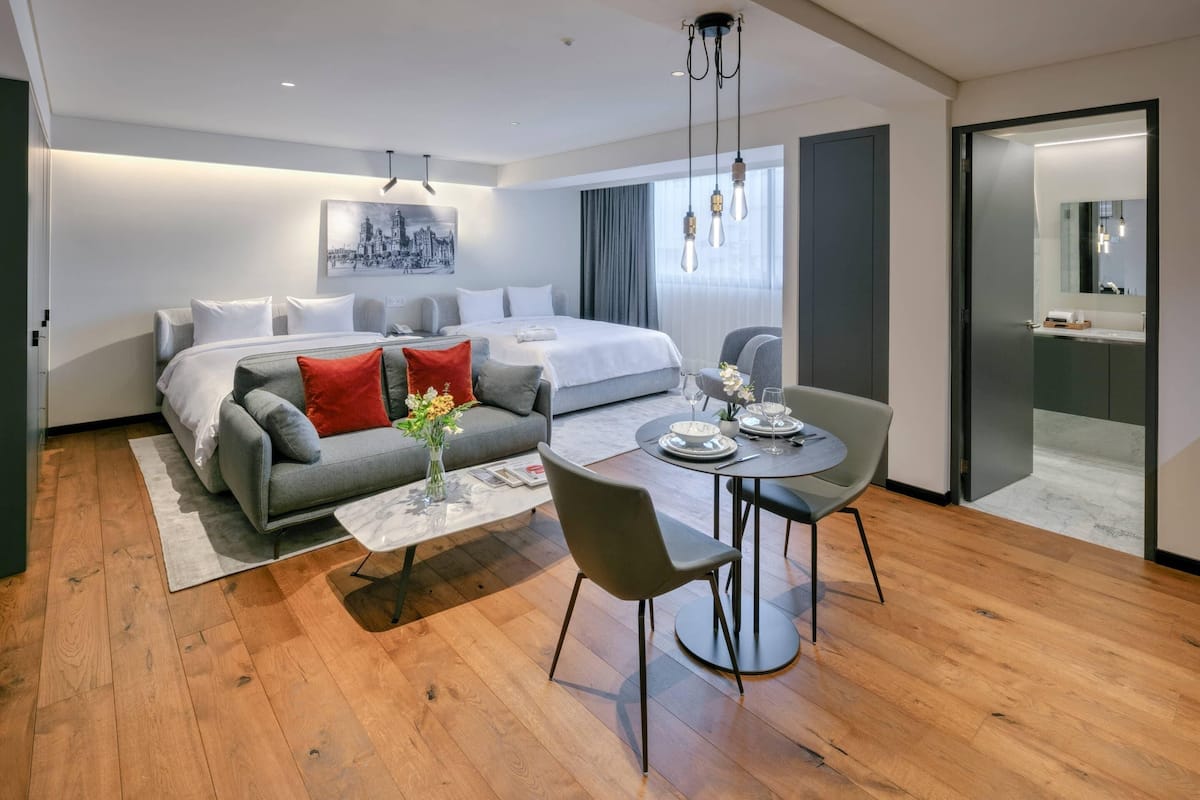A modern hotel room with a bed, sofa, dining table, and chairs.