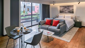 A modern hotel room with a large bed, grey sofa, and a dining area with a table and chairs. - Amberes 64, an Ascend Collection Hotel (Mexico City)