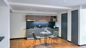 A modern kitchen with grey cabinets, a black countertop, and a dining area with two chairs and a table.