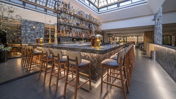 A spacious bar area with a high ceiling and skylight, featuring a long counter with stools and a well-stocked bar. - Amberes 64, an Ascend Collection Hotel (Mexico City)