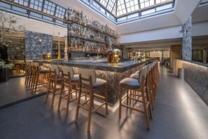 Un vaste espace bar doté d’un haut plafond et d’une verrière, avec un long comptoir agrémenté de tabourets et un bar bien fourni.