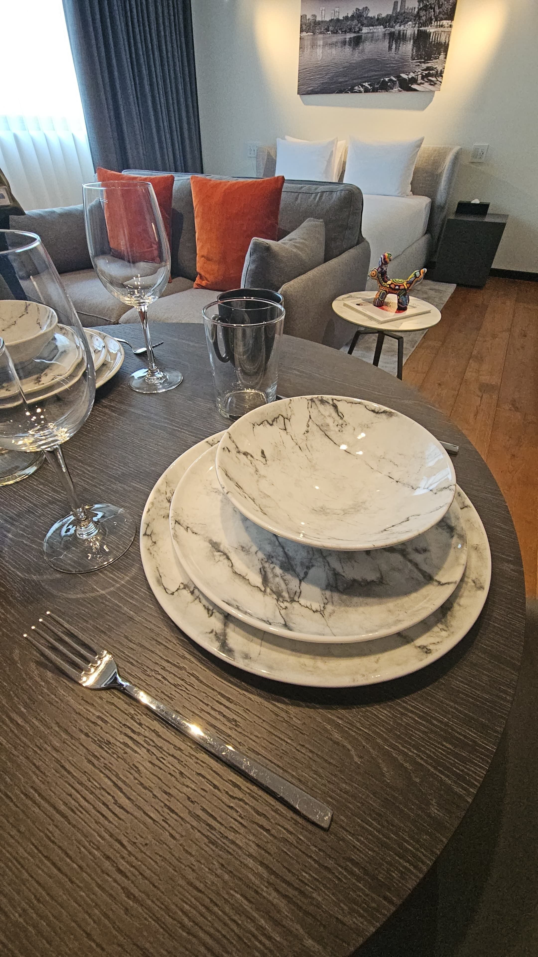 A dining table set with white marble plates, a fork, and wine glasses.
