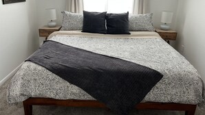 Cama bem arrumada com roupa de cama estampada, duas luminárias de cabeceira e um quadro na parede.