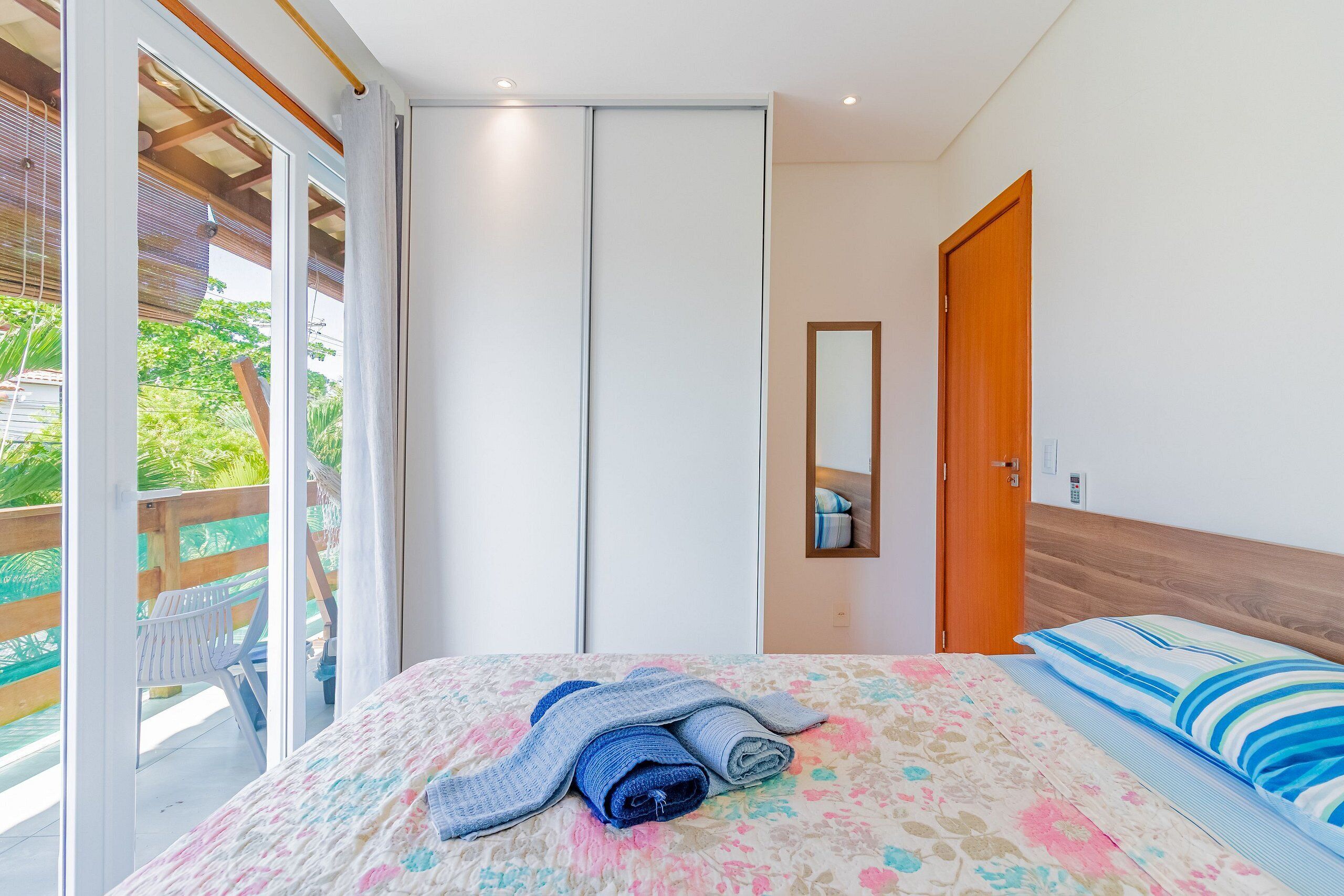 A bedroom with a bed, a wooden headboard, a mirror, and a sliding door leading to a balcony.