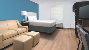 A modern hotel room with a bed, a sofa, a TV, and a window with blinds. - Woodspring Suites Rochester Greece (Rochester)