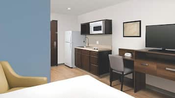 Una habitación de hotel compacta con kitchenette, una cama, un escritorio y una silla.