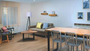 A modern living room with a sofa, a coffee table, a dining table with chairs, a floor lamp, and wall-mounted picture frames. - Woodspring Suites Rochester Greece (Rochester)