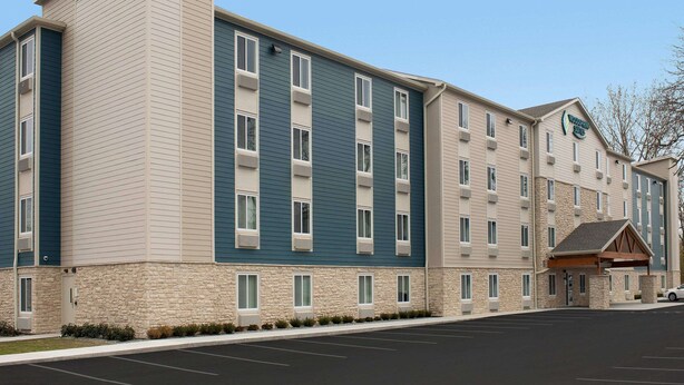 A multi-story hotel with a stone facade, multiple windows, and a parking lot. - Woodspring Suites Rochester Greece (Rochester)
