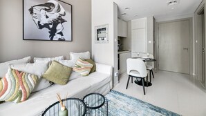 A modern living room with a white sofa, a dining area with a table and chairs, and a kitchen visible in the background. - Heavenly New 1 BD in Business Bay (Dubai)