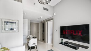 A modern hotel room with a large flat-screen TV mounted on the wall, a dining area with a table and chairs, and a cozy seating area with a sofa and a patterned rug. - Heavenly New 1 BD in Business Bay (Dubai)