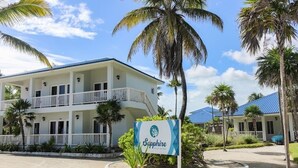 Een meerlaags hotel met een witte gevel en balkons, omringd door palmbomen en een heldere lucht.