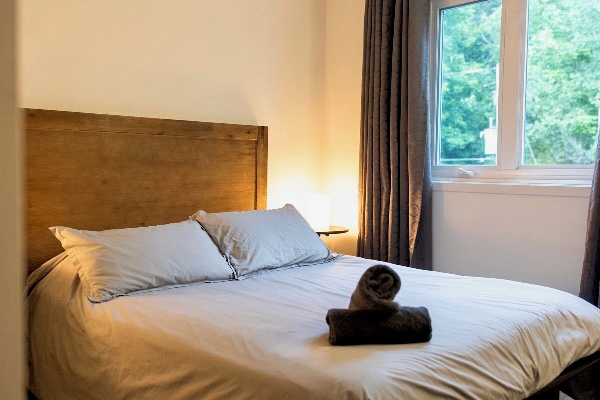 A neatly made bed with a wooden headboard, white bedding, and a rolled towel on the bed.