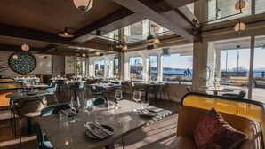 Un restaurante espacioso con numerosas mesas, amplias ventanas que ofrecen vistas al exterior y una combinación de decoración moderna y tradicional.