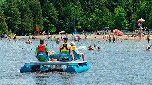 Un lago con gente en botes a pedales y otros nadando y tomando el sol en la orilla.