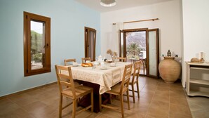 Comedor con una mesa preparada para cuatro personas, sillas de madera, un jarrón grande y vistas a través de una puerta abierta.