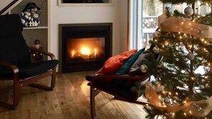 A cozy living room with a fireplace, a television mounted on the wall, a Christmas tree, and a staircase. - Le Cocoon 5 minutes from Mont Orford and Magog (Orford)