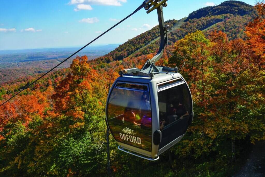 Une télécabine portant l’inscription « MONT-ORFORD », suspendue au-dessus d’un paysage boisé.