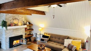 Una sala de estar tipo loft acogedora con vigas de madera a la vista, una chimenea de piedra y un sofá cómodo con cojines.