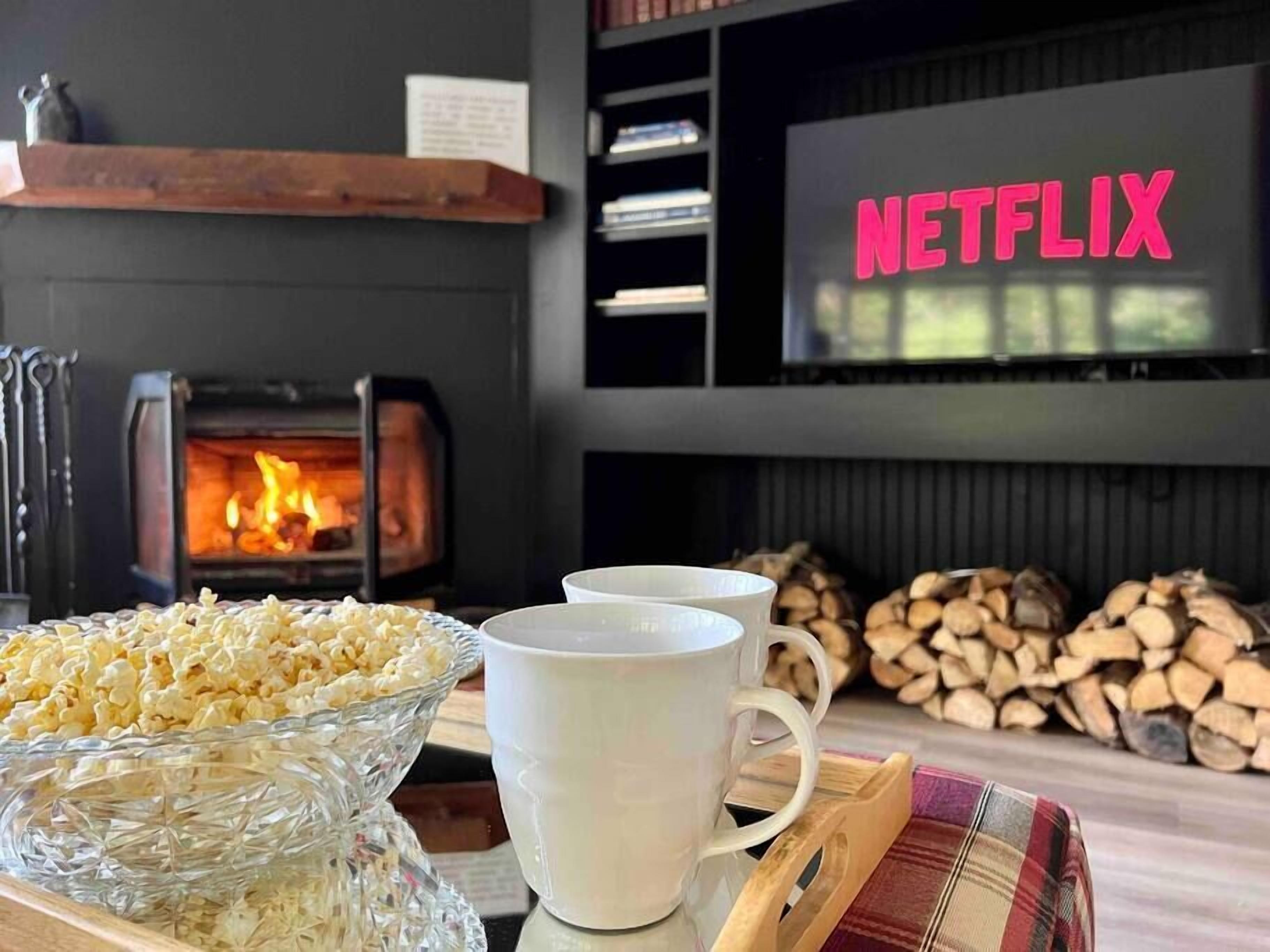 Una sala de estar acogedora con chimenea, un letrero de Netflix, palomitas de maíz y dos tazas.