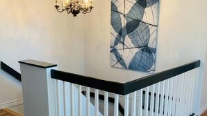 Una escalera con barandilla blanca, superficie negra y un candelabro colgante.