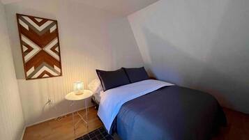 Un dormitori amb un llit, una tauleta de nit amb una làmpada, una decoració mural amb motius i un sòl de fusta.