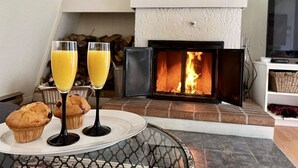 A cozy living room with a fireplace, a coffee table with muffins and glasses, and a television on a stand. - The Jackrabbit (Mount Orford) (Orford)