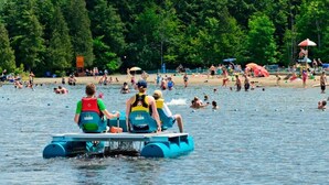 Un lago con gente en una balsa azul, y otros nadando y tomando el sol en la orilla.