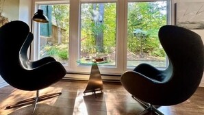 Una habitación de diseño moderno, con dos sillas negras, una mesa y grandes ventanales que ofrecen vistas a zonas verdes.