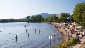 A lakeside beach with people swimming and sunbathing, a gazebo, and buildings in the background. - A favorite chalet in Orford (Orford)