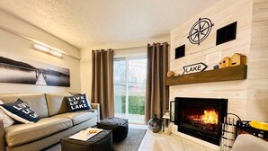 A modern living room with a fireplace, a sofa, a coffee table, and a large window with curtains. - Merry Sud  Suite-Condo with Indoor Pool and Spa (Magog)