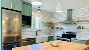 Eine moderne Küche mit grünen Schränken, Edelstahlgeräten und einer Holztischinsel.