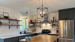 Cozinha moderna com ilha de madeira, eletrodomésticos de aço inoxidável e armários em preto.