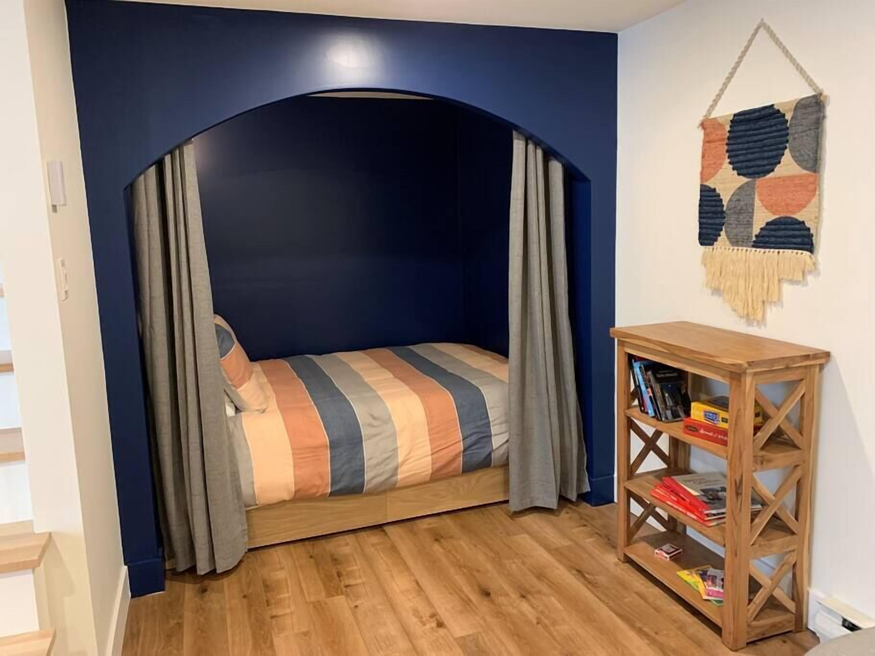 Une pièce chaleureuse avec un lit placé sous un plafond cintré, une bibliothèque en bois et une décoration murale en macramé.