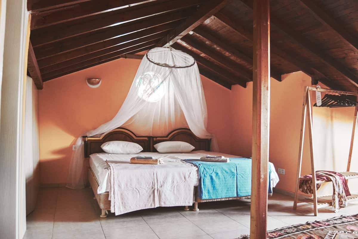 Een slaapkamer met een bed onder een klamboe, een houten plafond en een stoel met een plaid.
