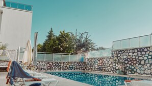 A swimming pool with lounge chairs and umbrellas, surrounded by a stone wall and a building with a balcony. - Villa Nordic Dream (Kas)