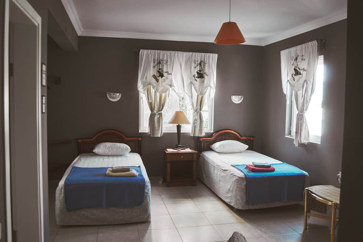 Een kamer met twee éénpersoonsbedden, een nachtkastje met een lamp en een stoel.