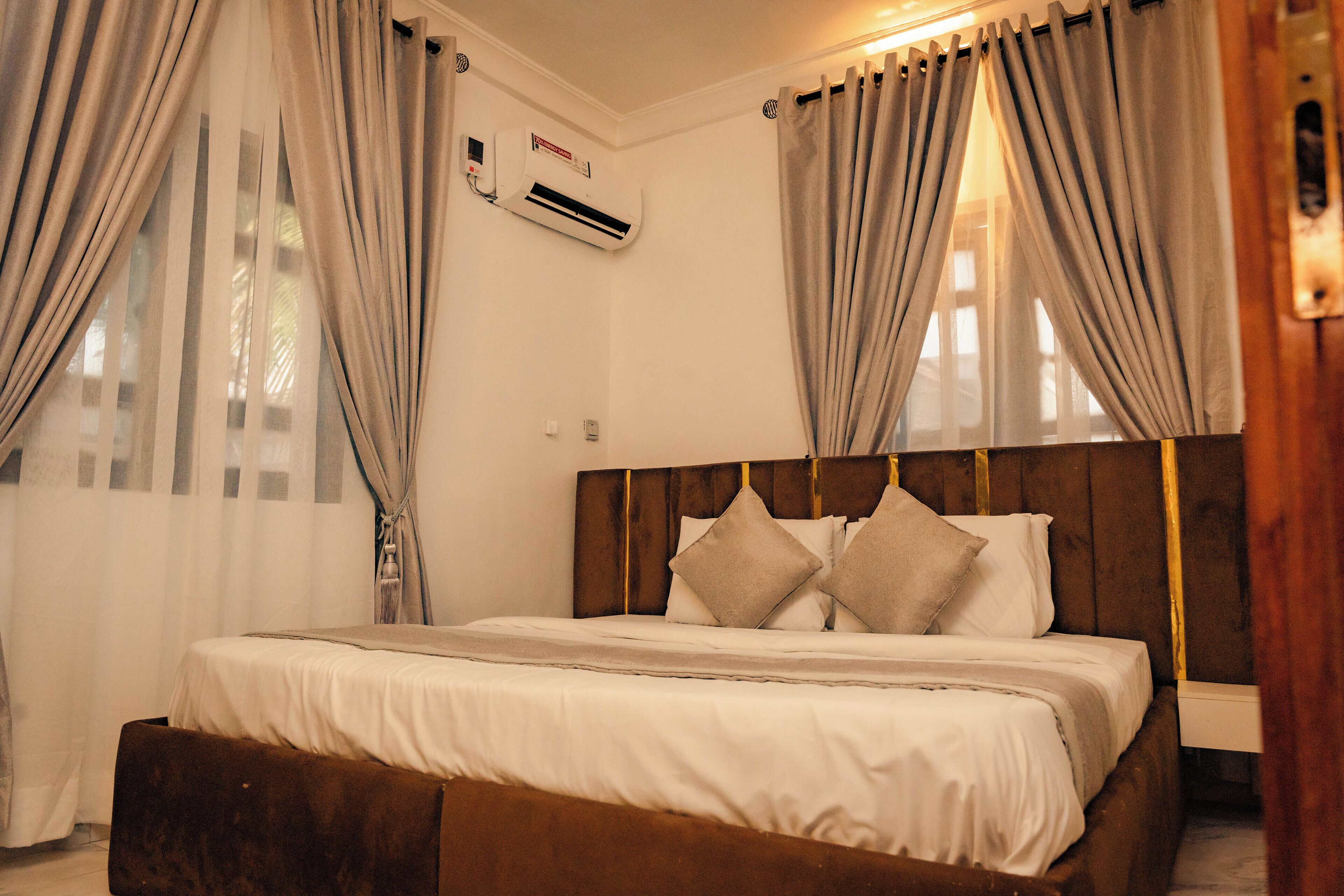 A neatly made bed with a wooden headboard, a bedside table, and a wall-mounted air conditioning unit.