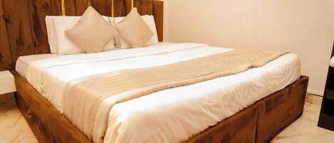 A neatly made bed with a wooden headboard, white bedding, and a beige throw blanket.