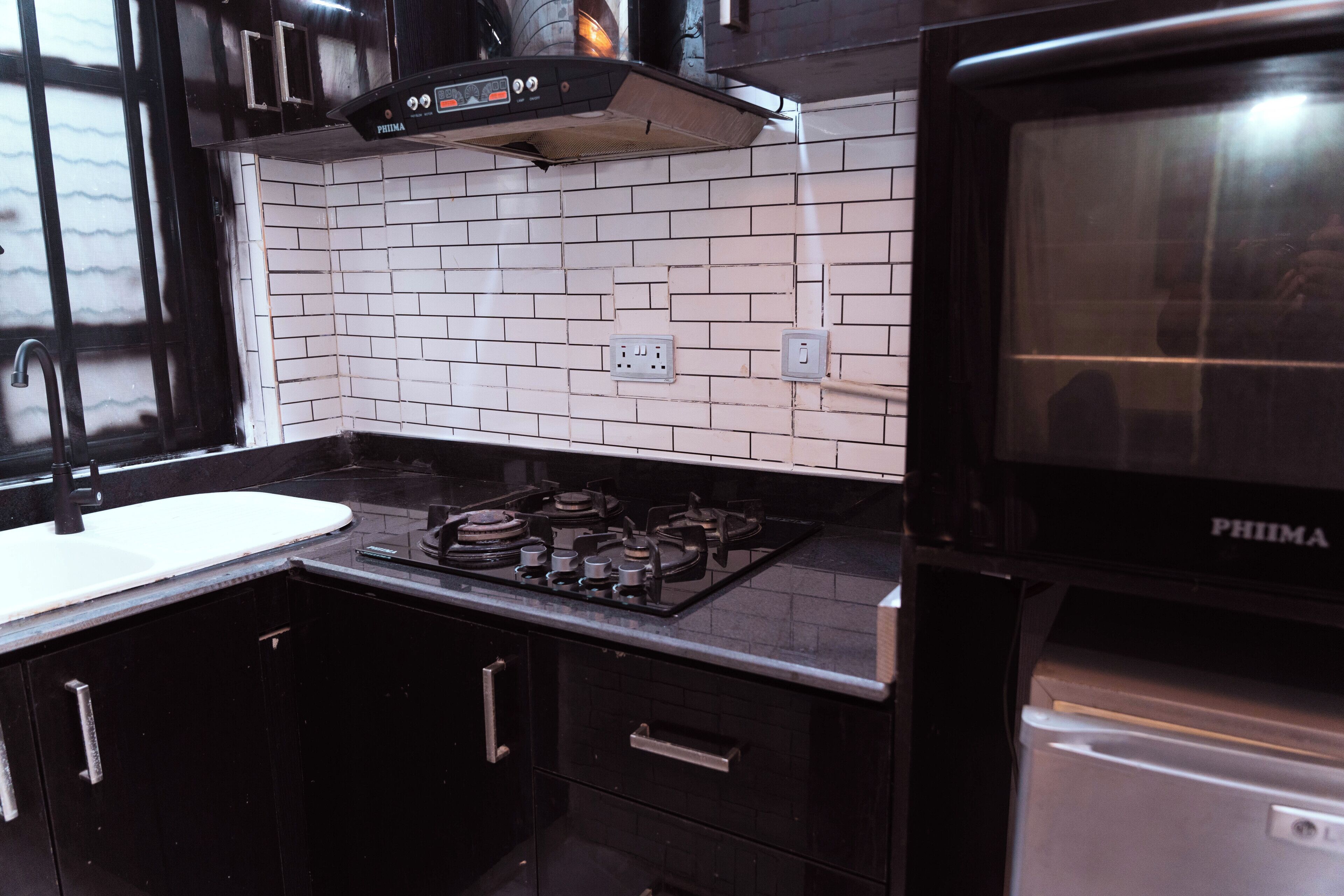A kitchen with a gas stove, black cabinets, a white tiled backsplash, and a PHIMA oven.