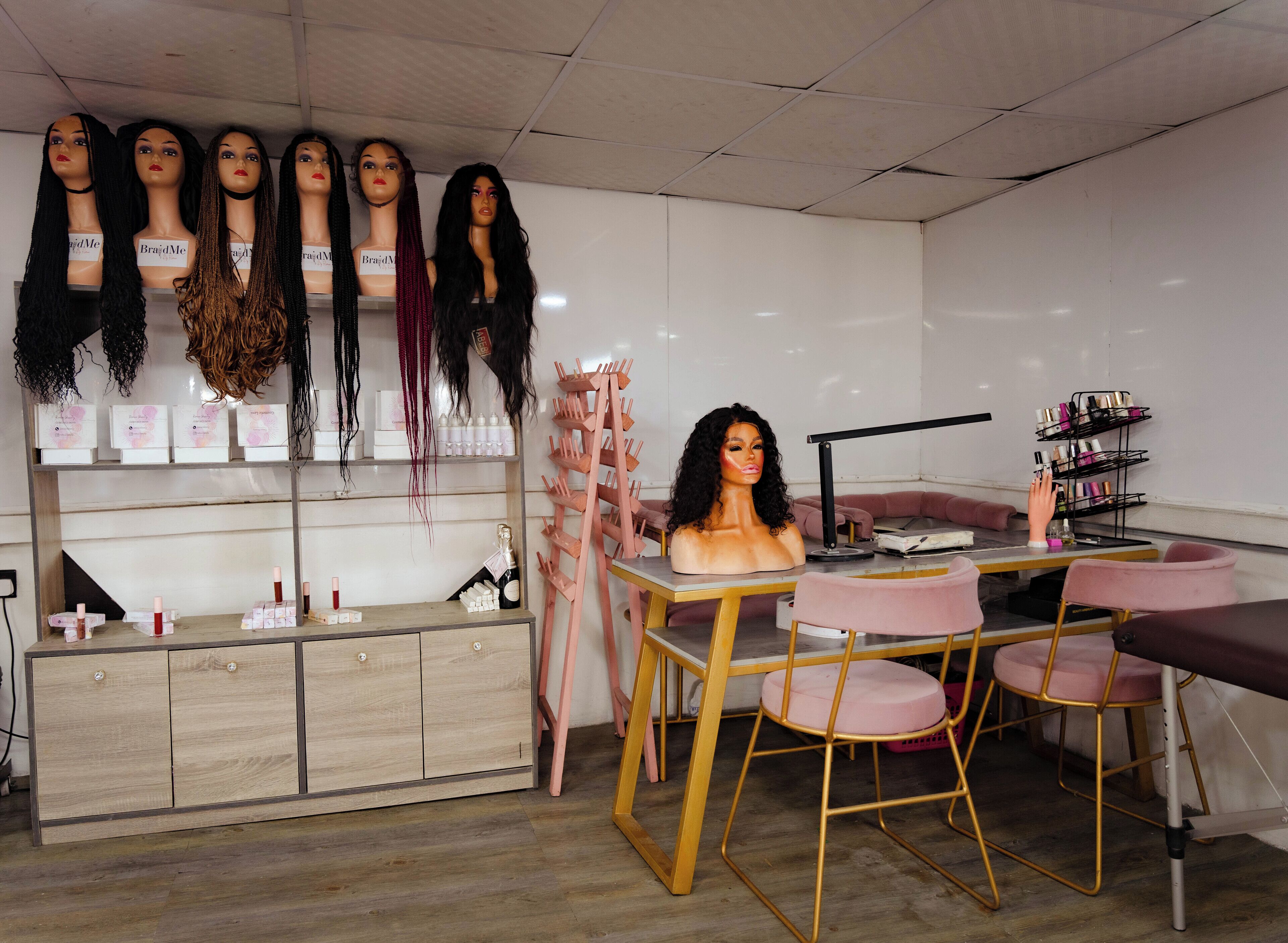 A salon with multiple mannequin heads displaying wigs, a vanity table with hair products, and pink chairs.
