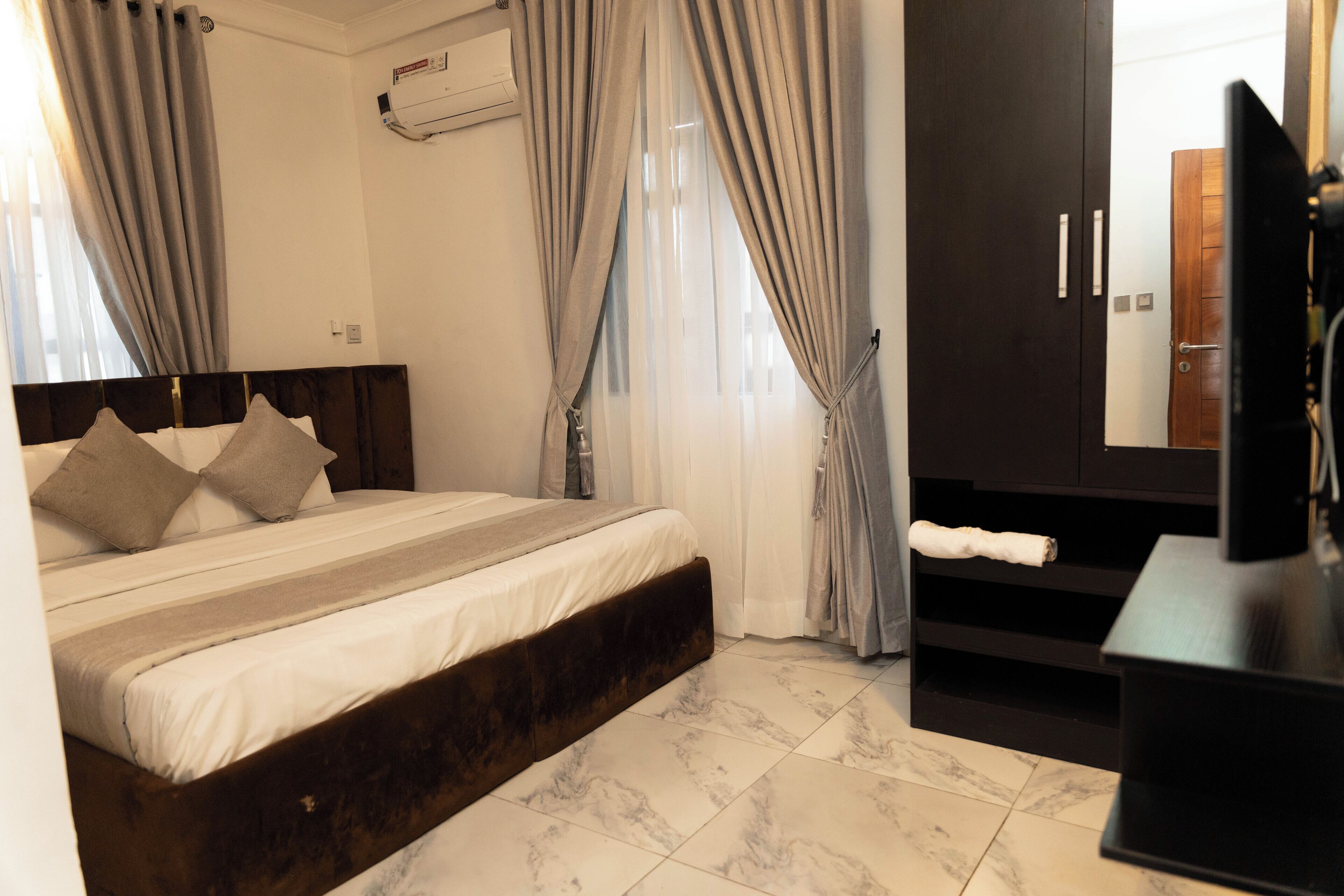 A bedroom with a bed, curtains, a TV, and a wardrobe.