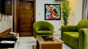 A modern living room with a wooden door, green armchairs, a coffee table, and a painting on the wall. - 247 Luxury Apartment (Lekki)