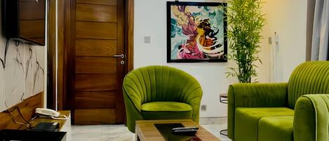Una sala de estar moderna con una puerta de madera, sillones verdes, una mesa de centro y un cuadro en la pared.