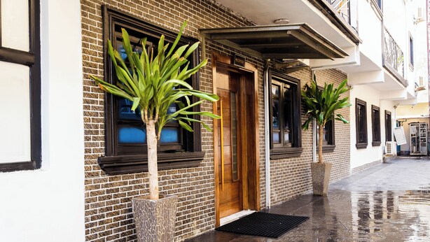 A brick building with a wooden door and windows, potted plants, and a wet pavement. - 247 Luxury Apartment (Lekki)