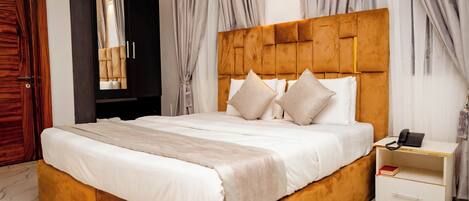 Un dormitorio con una cama grande, cabecera de madera, una mesita de noche, un espejo y cortinas.