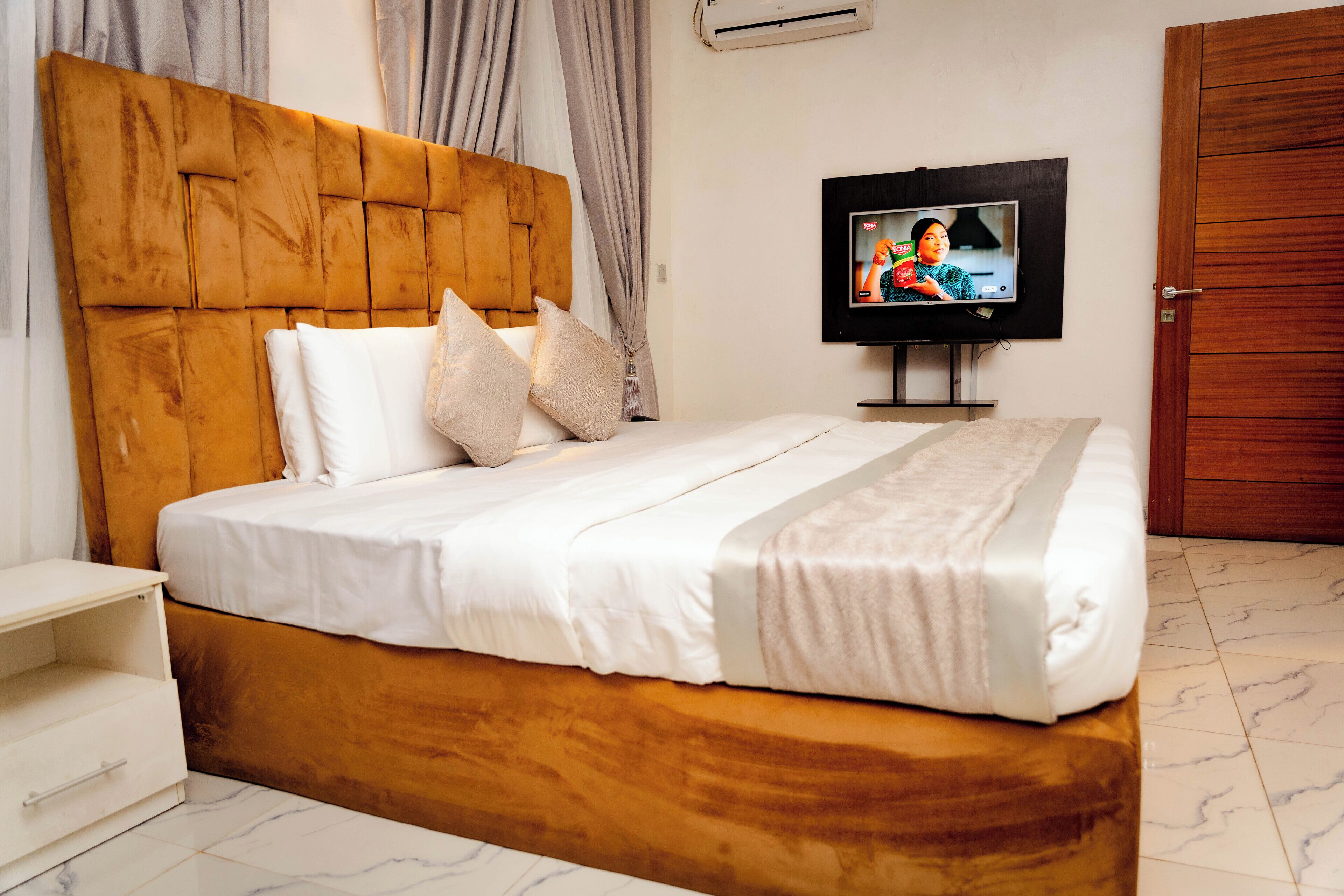 A neatly made bed with a wooden headboard, a television on a stand, and a wooden wardrobe in a hotel room.
