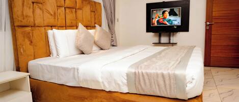 A neatly made bed with a wooden headboard, a television on a stand, and a wooden wardrobe in a hotel room.