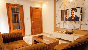 A living room with a wooden door, a television mounted on the wall, a sofa, and a coffee table. - 247 Luxury Apartment (Lekki)