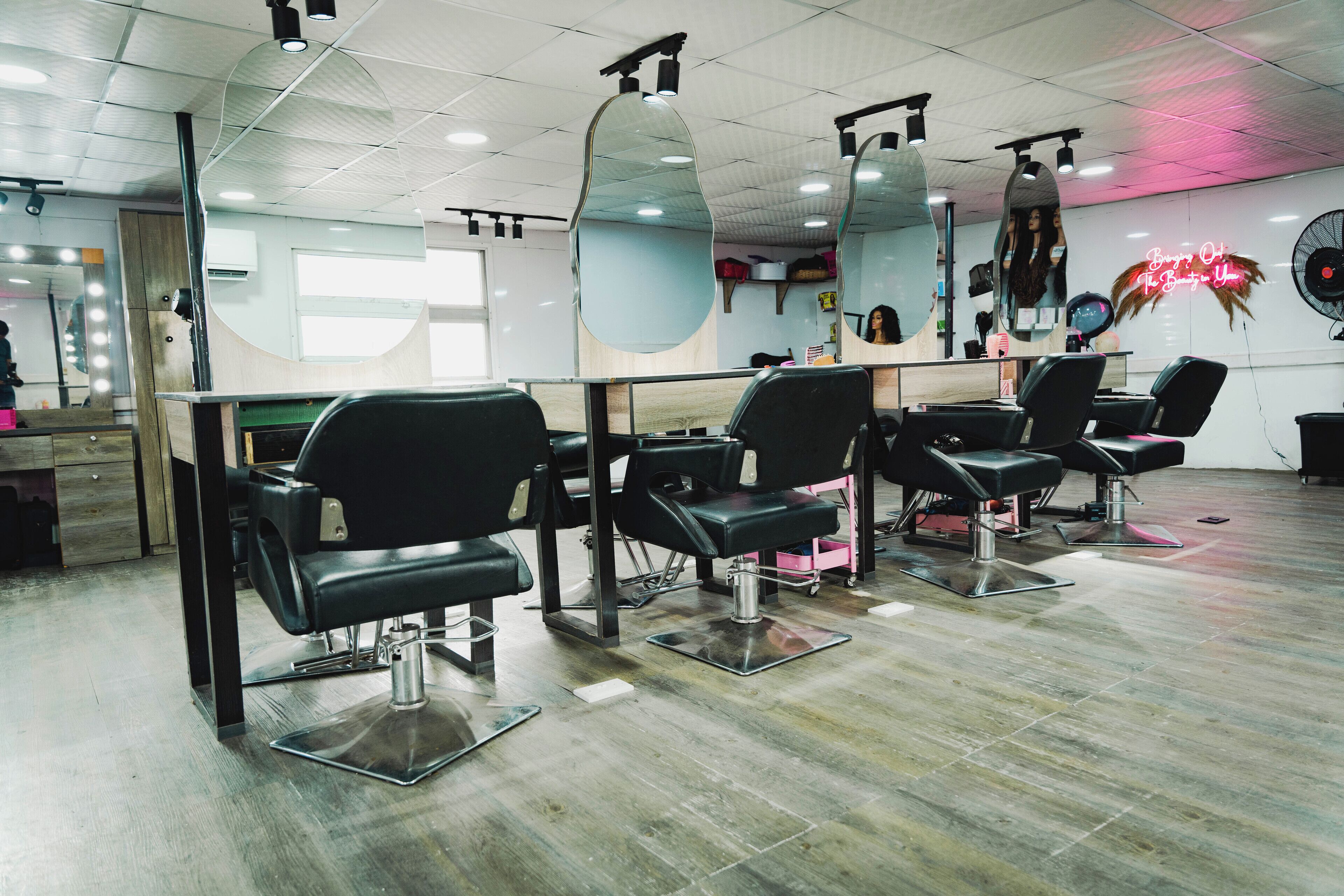 A salon with multiple black salon chairs, a mirror, and a neon sign on the wall.